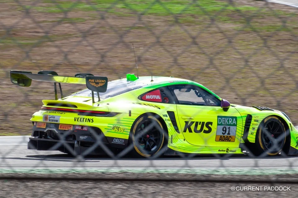 Yellow and green Porsche number 91 seen through trackside fencing