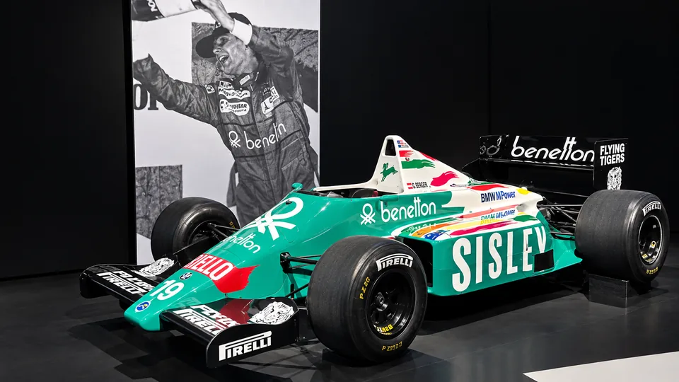 Green and white Benetton Formula 1 car displayed beside a black and white victory photograph