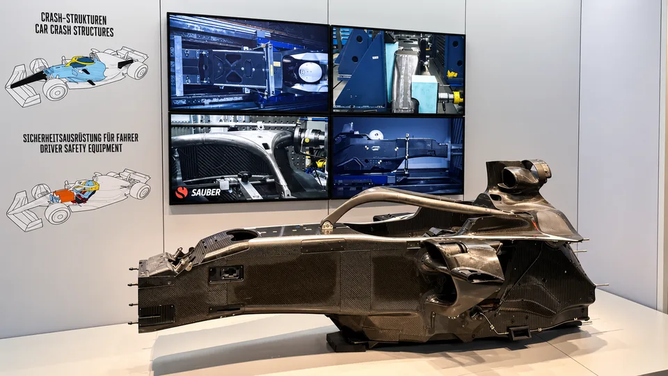 Bare carbon Formula 1 chassis displayed beside screens explaining crash structures
