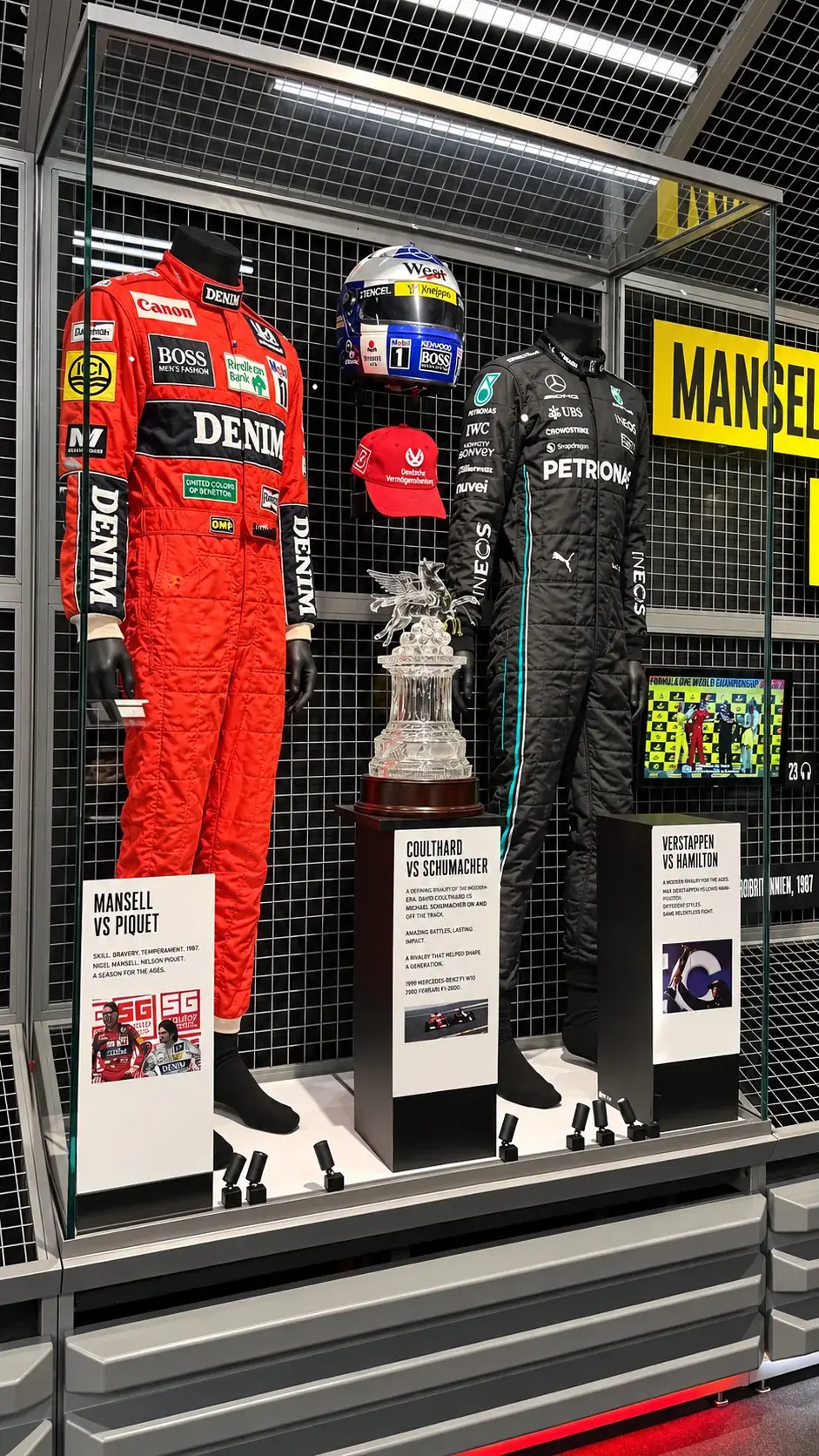 Glass case holding two race suits, a helmet and a trophy from famous rivalries