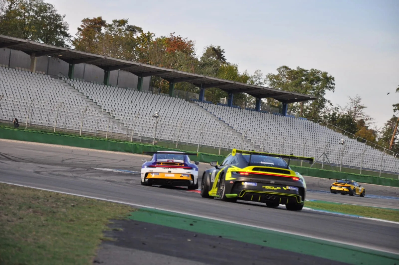 Two Porsche 911 race cars rounding a corner below an empty grandstand