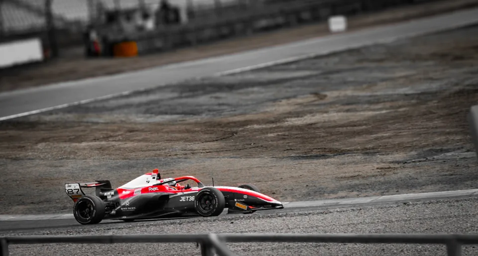 Red and white number 87 single-seater on track, the surroundings drained of colour