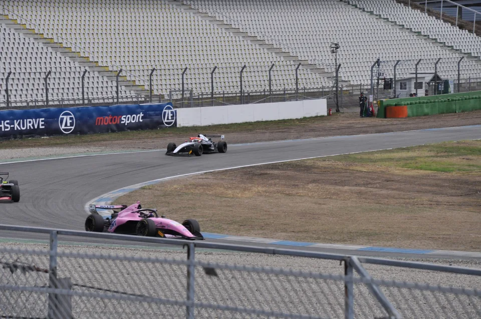 Pink and white single-seaters running line astern through the Sachs-Kurve