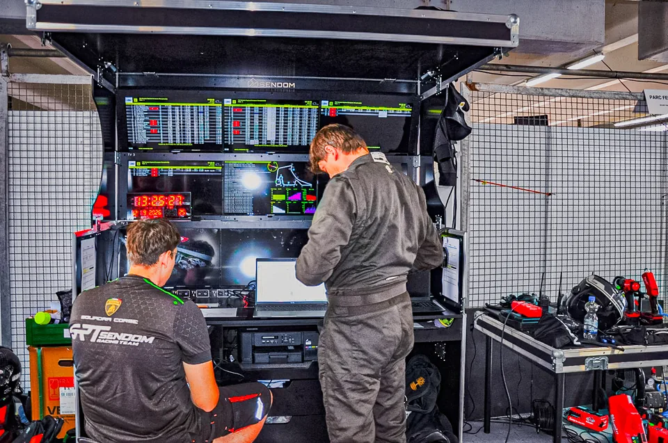 Two team members working at a timing stand with live timing screens and a lap chart