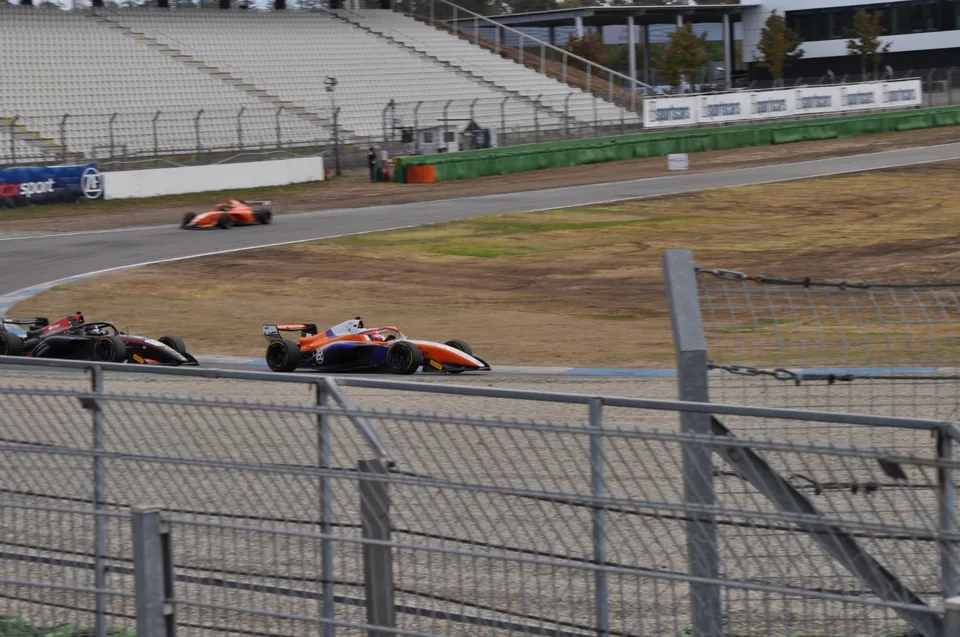 Orange and black single-seaters seen through the trackside catch fencing