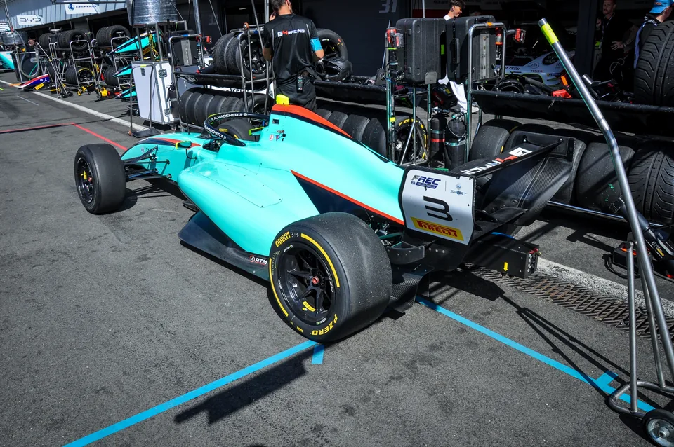 Turquoise number 3 Formula Regional car sitting in its pit box with tyres and equipment around it