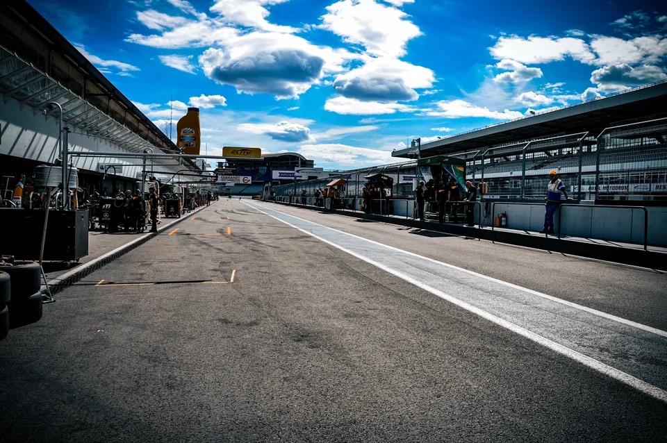 View down the Hockenheimring pit lane under a bright blue sky with teams working at their boxes