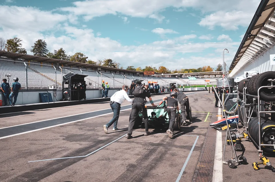 Team members pushing a single-seater race car along the pit lane