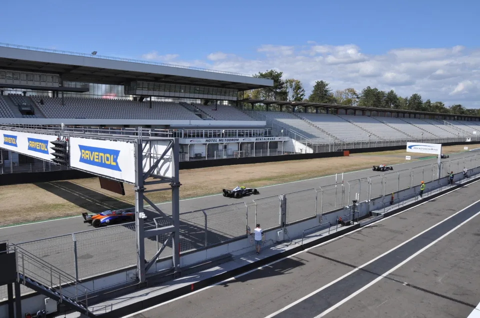 Elevated view of the main straight with cars passing the Hotel Motodrom grandstand
