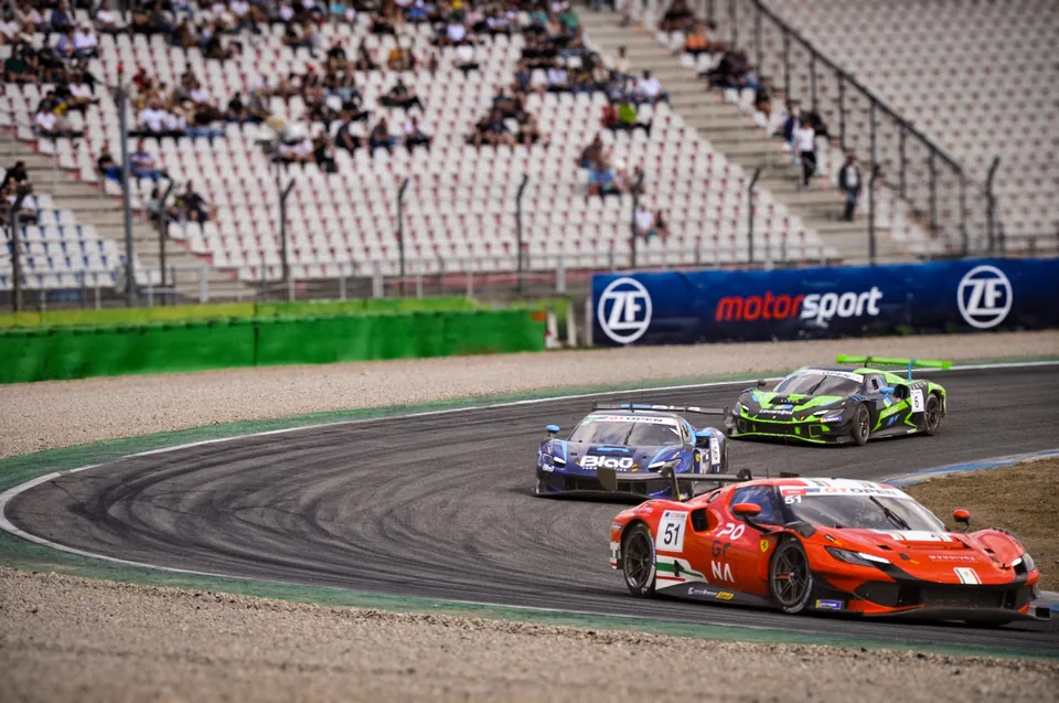 Number 51 Ferrari 296 GT3 leading a blue Ferrari and a green Lamborghini through a corner in front of the grandstand