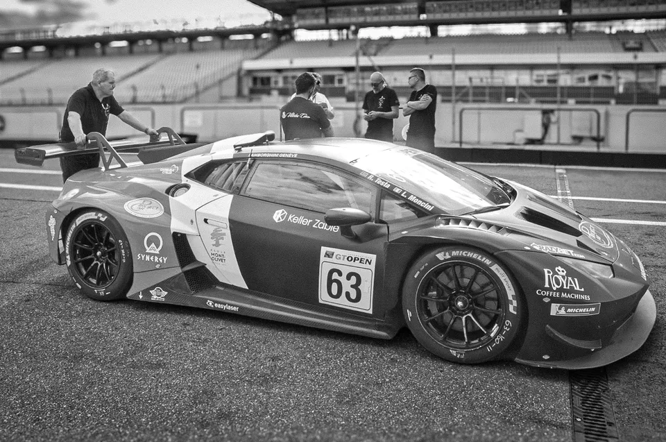 Black and white photograph of the number 63 Lamborghini Huracán GT3 with crew members standing behind it
