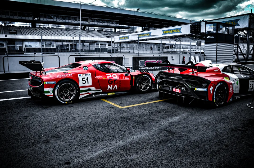 Red number 51 Ferrari and number 63 Lamborghini standing in the pit lane under heavy cloud