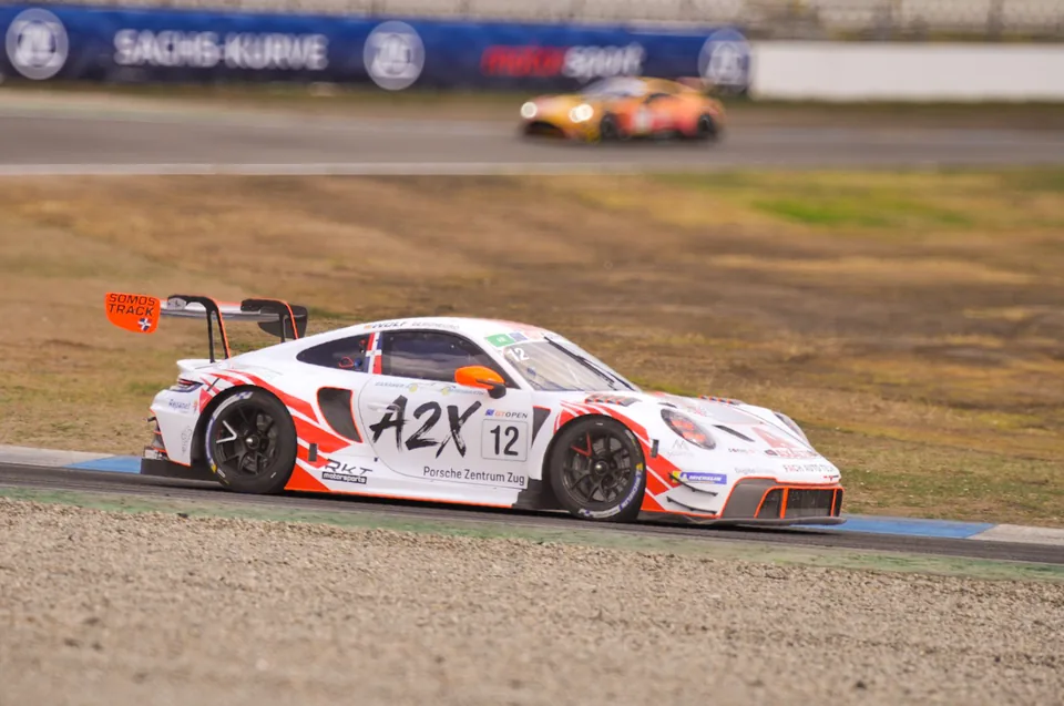 White and orange number 12 Porsche 911 GT3 R cornering at the Sachs-Kurve