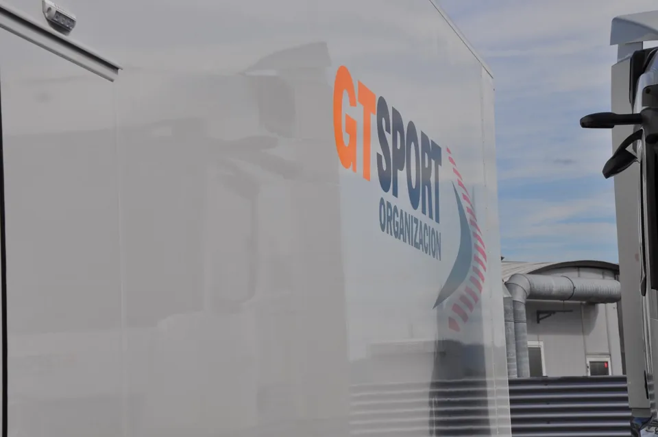Side panel of a white series transporter carrying the GT Sport Organizacion logo against a blue sky