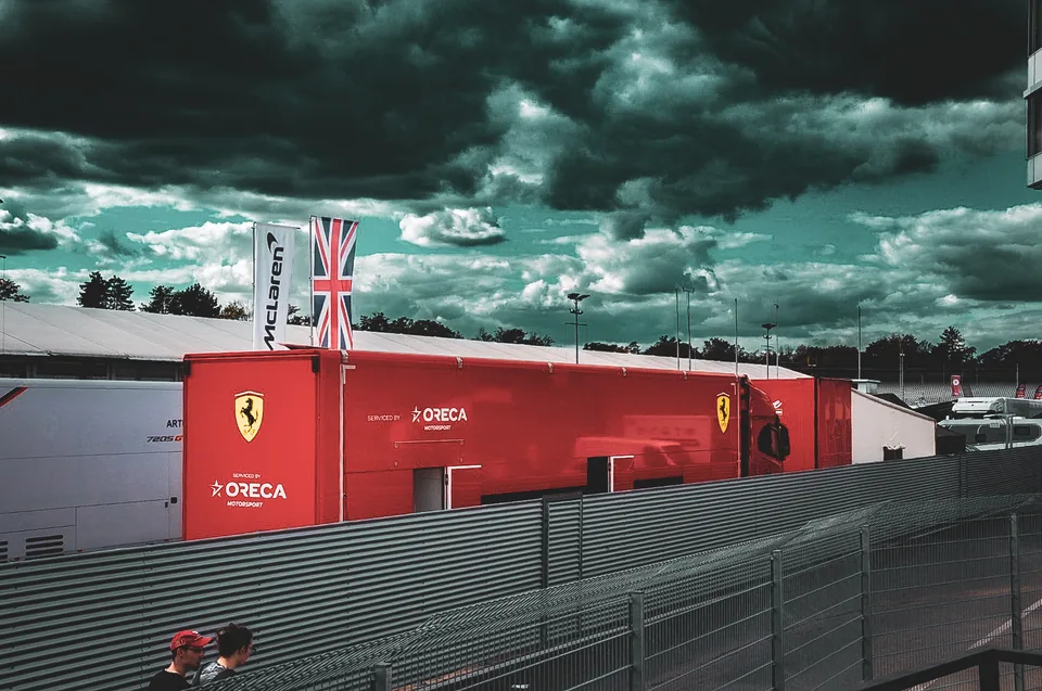 Red team transporter with flags flying in the paddock beneath dark storm clouds