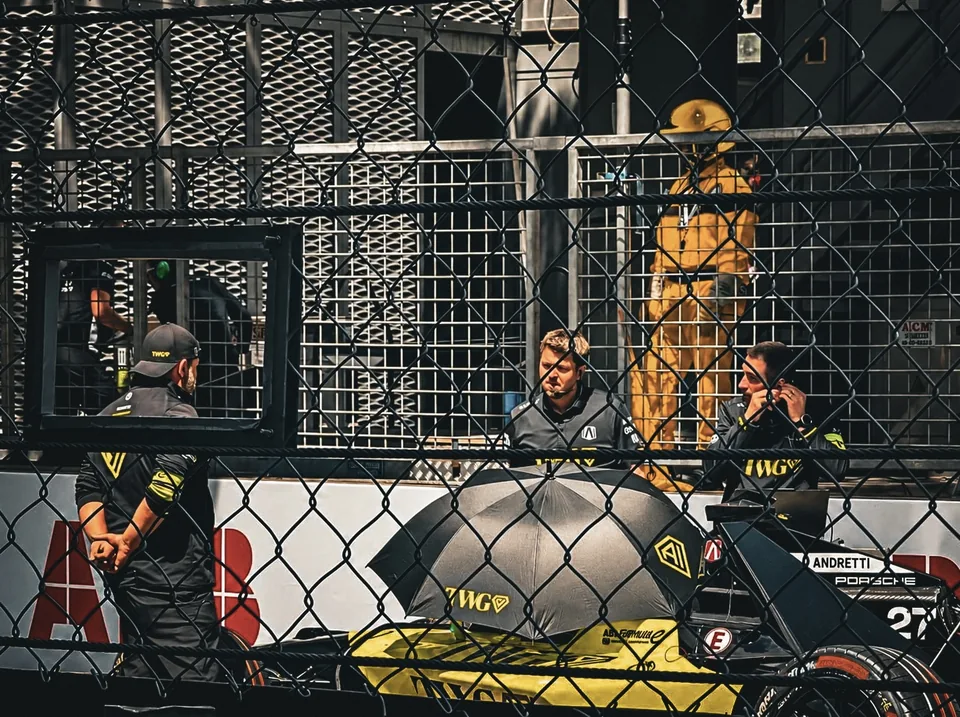 Team members standing around a Formula E car shaded by a large umbrella