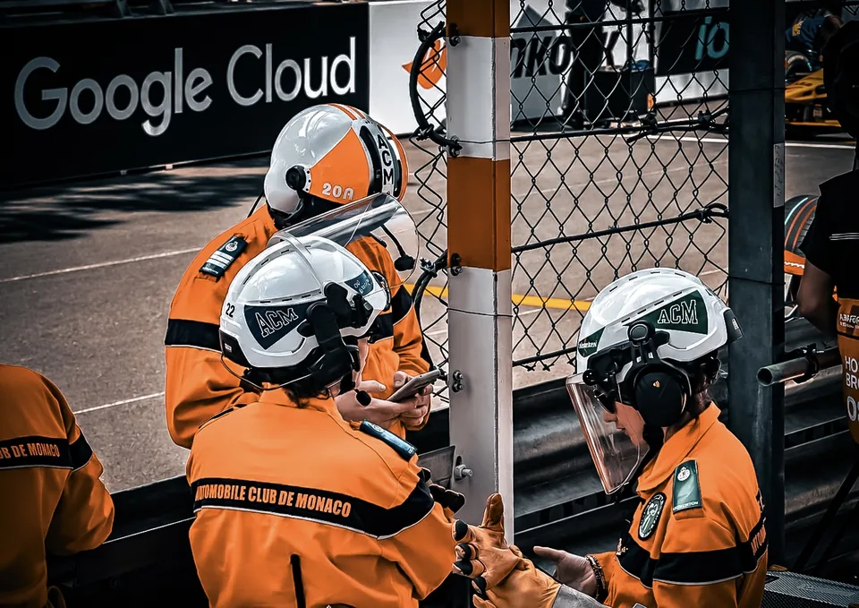 Three marshals in orange overalls and white helmets at a trackside post in Monaco