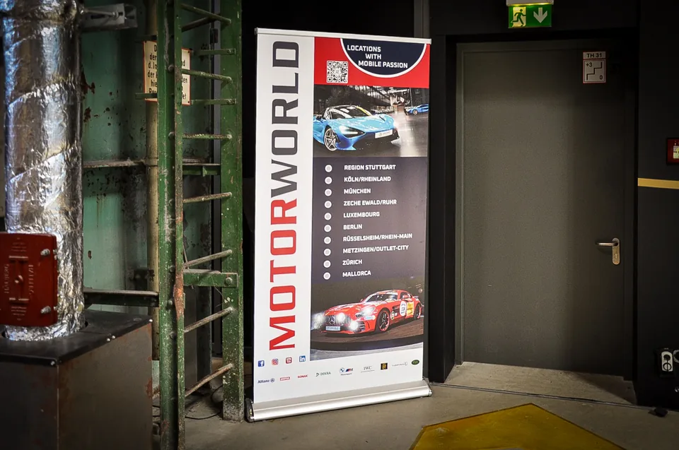 Motorworld roll up banner standing beside industrial pipework and a fire door