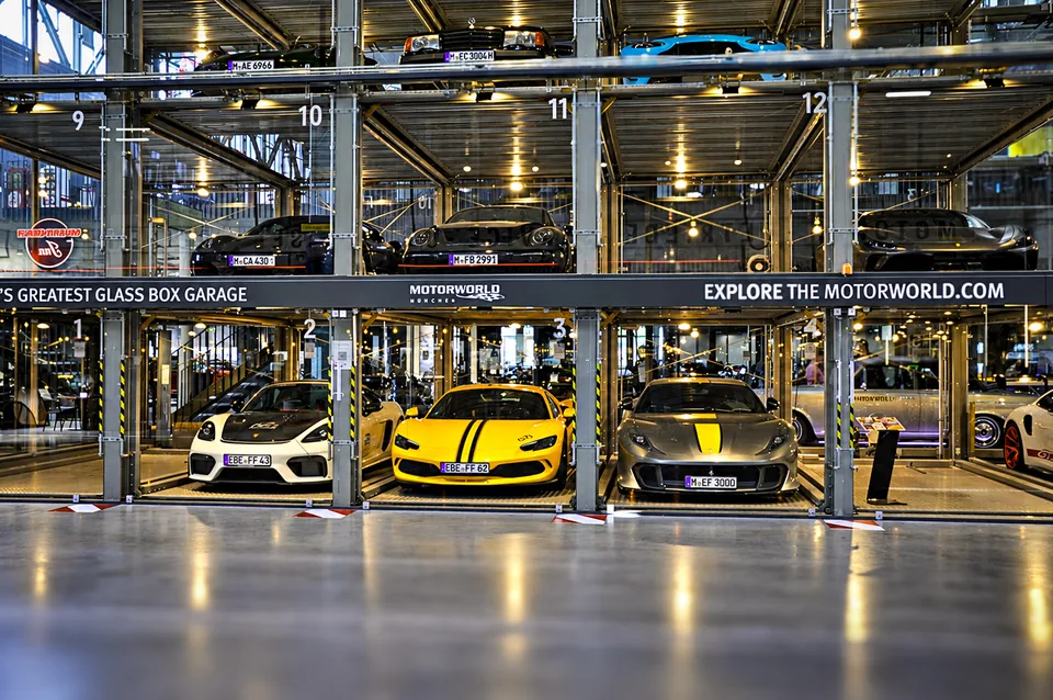 Multi level glass box garage stacked with sports cars under warm indoor lighting