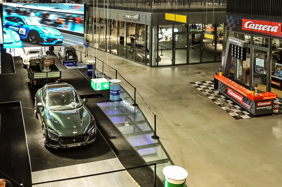 Elevated view across the Motorworld hall with display cars, shop fronts and a large screen