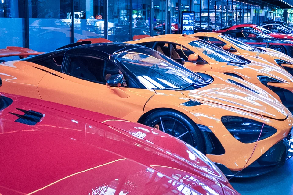 Row of orange and red McLaren supercars parked nose to tail behind glass