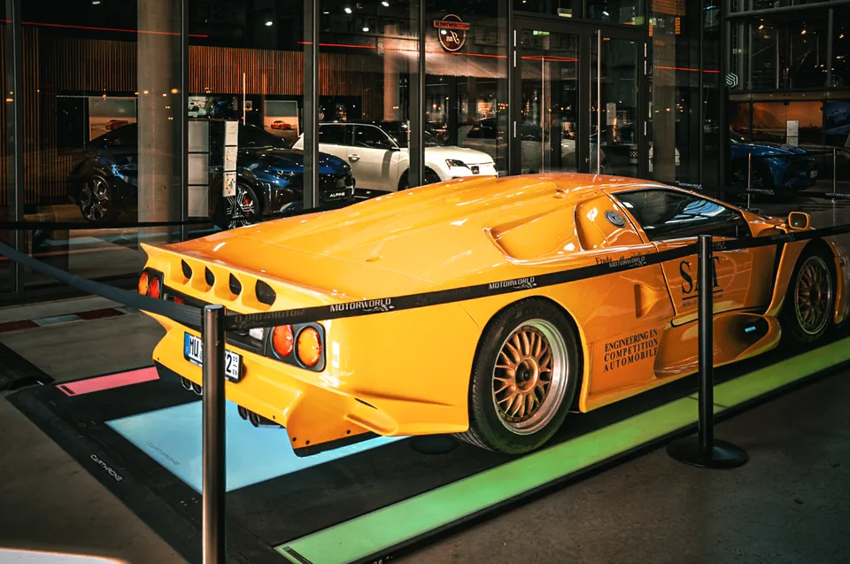 Yellow nineteen nineties GT racing car displayed behind a rope barrier at night